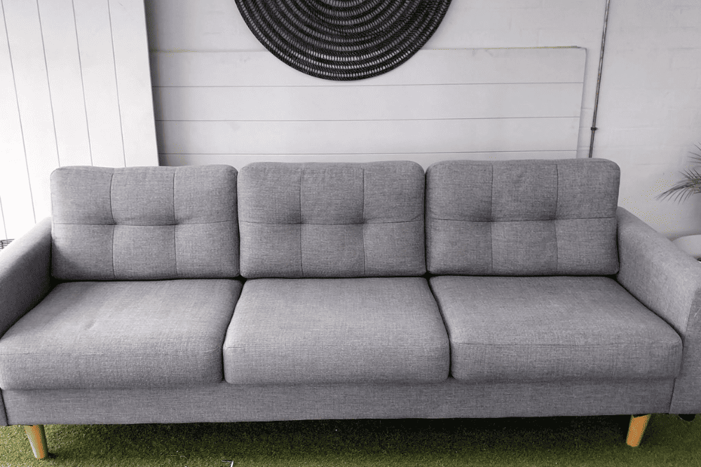A three-seater grey fabric couch thoroughly cleaned and sitting indoors-